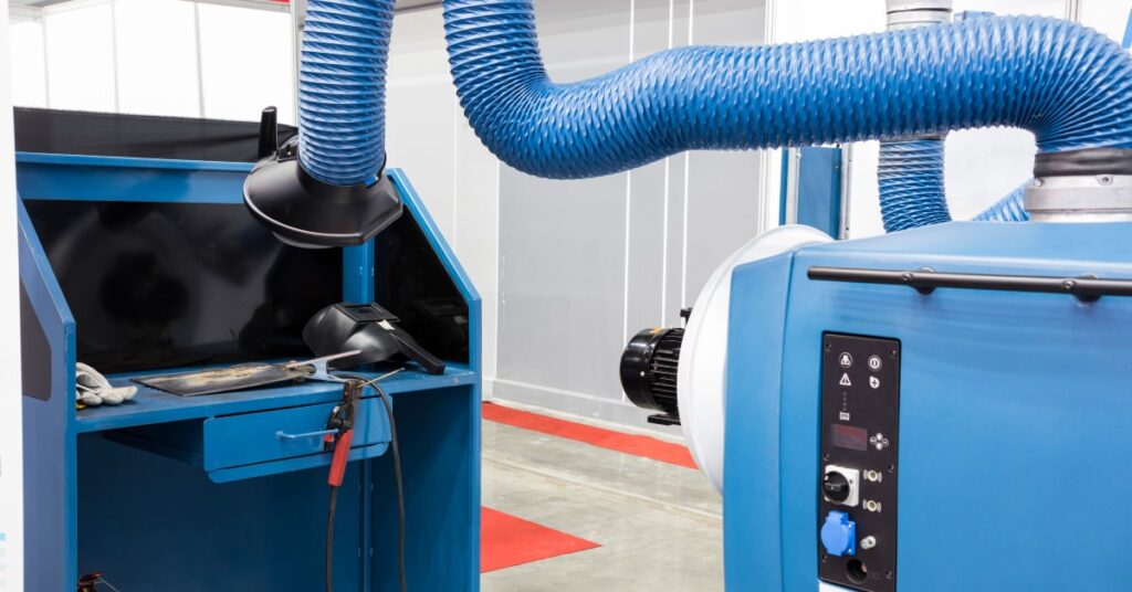 A welding fume extractor has its long tube extended outward and over a workstation. Both the extractor and station are blue.
