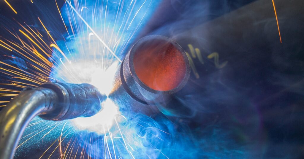 Close-up of a welding tool generating sparks as it touches metal. Yellow and white sparks shoot out.