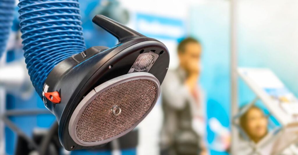 Close-up of a blue welding fume extractor with a filter on the end. Two people stand nearby, in the background.