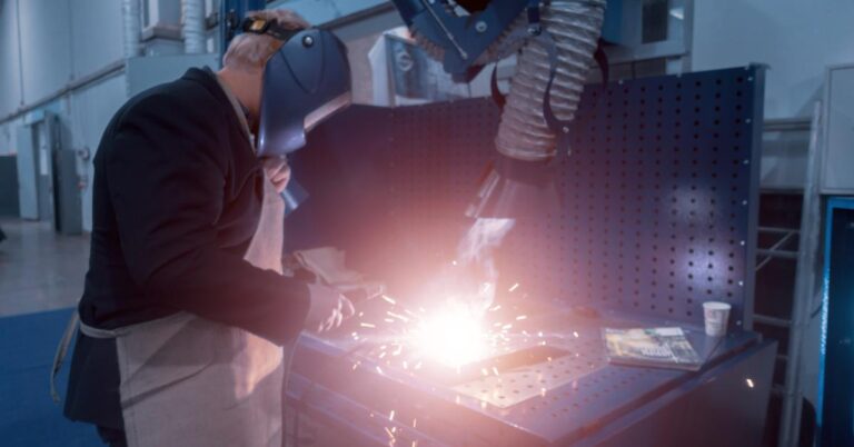 A worker wearing a safety mask welds in a factory. An extractor removes the smoke from the work environment.